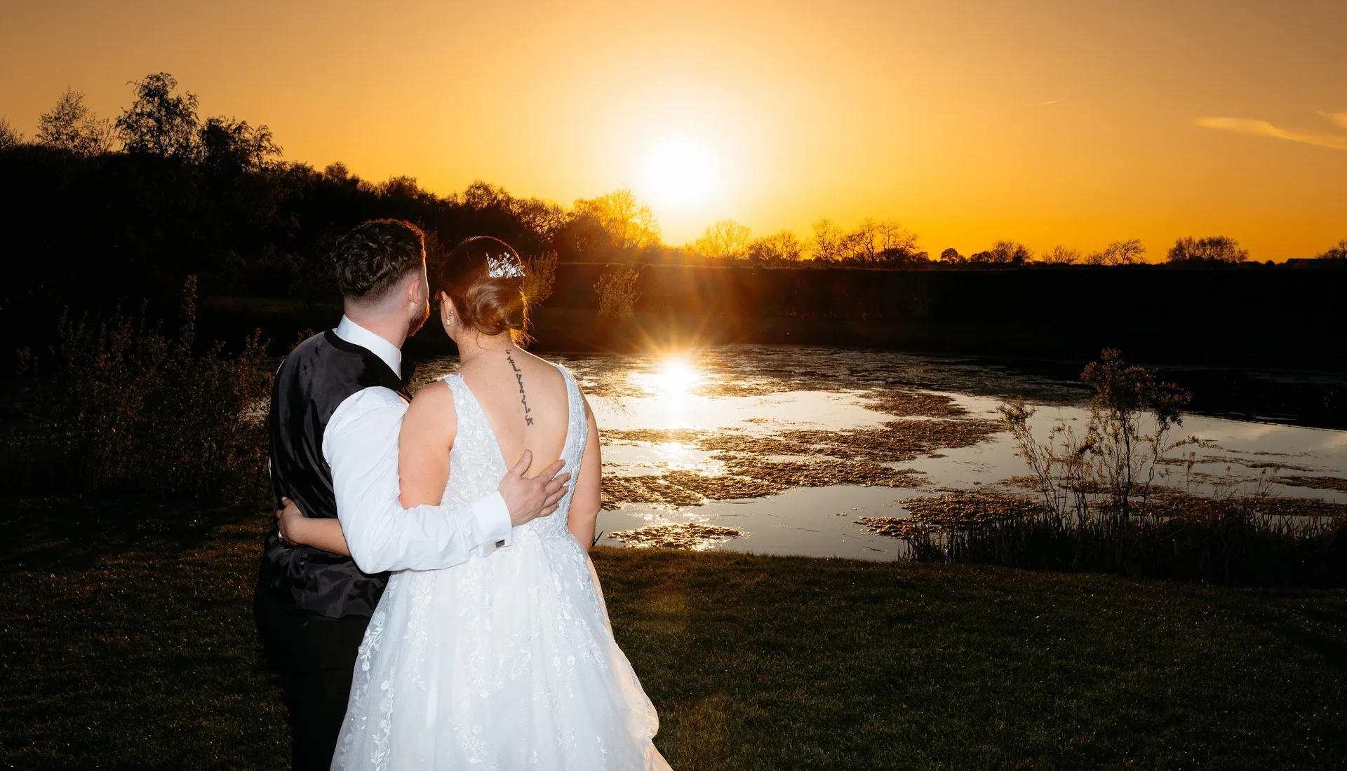 A couple by the lake as the sun sets at The Hidden Oak.