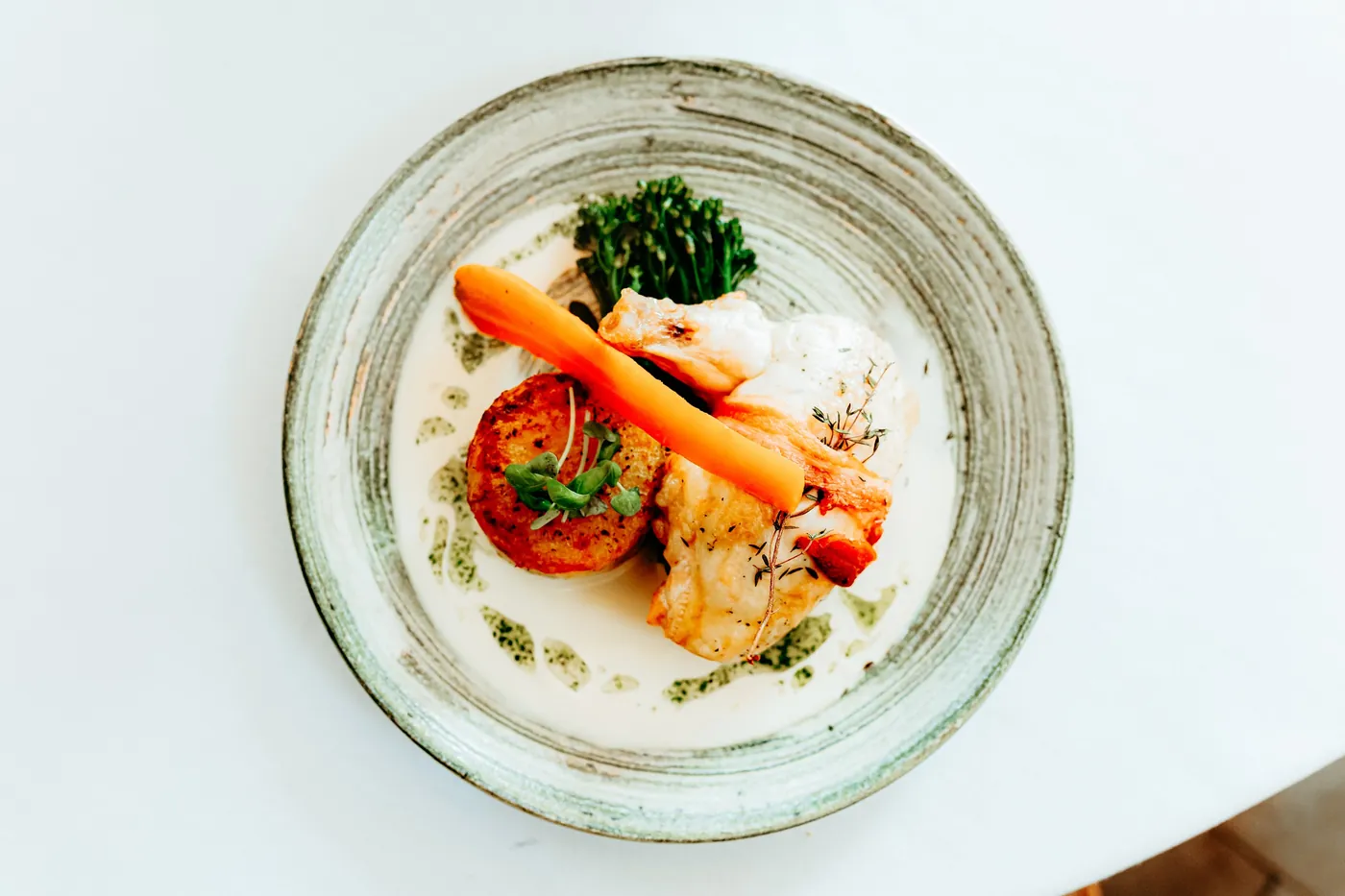 Scallop and fish plated with carrot and broccolini
