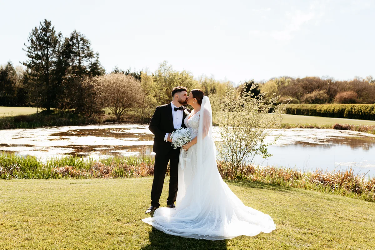 A couple beside the lake, with the grounds and woodland behind.