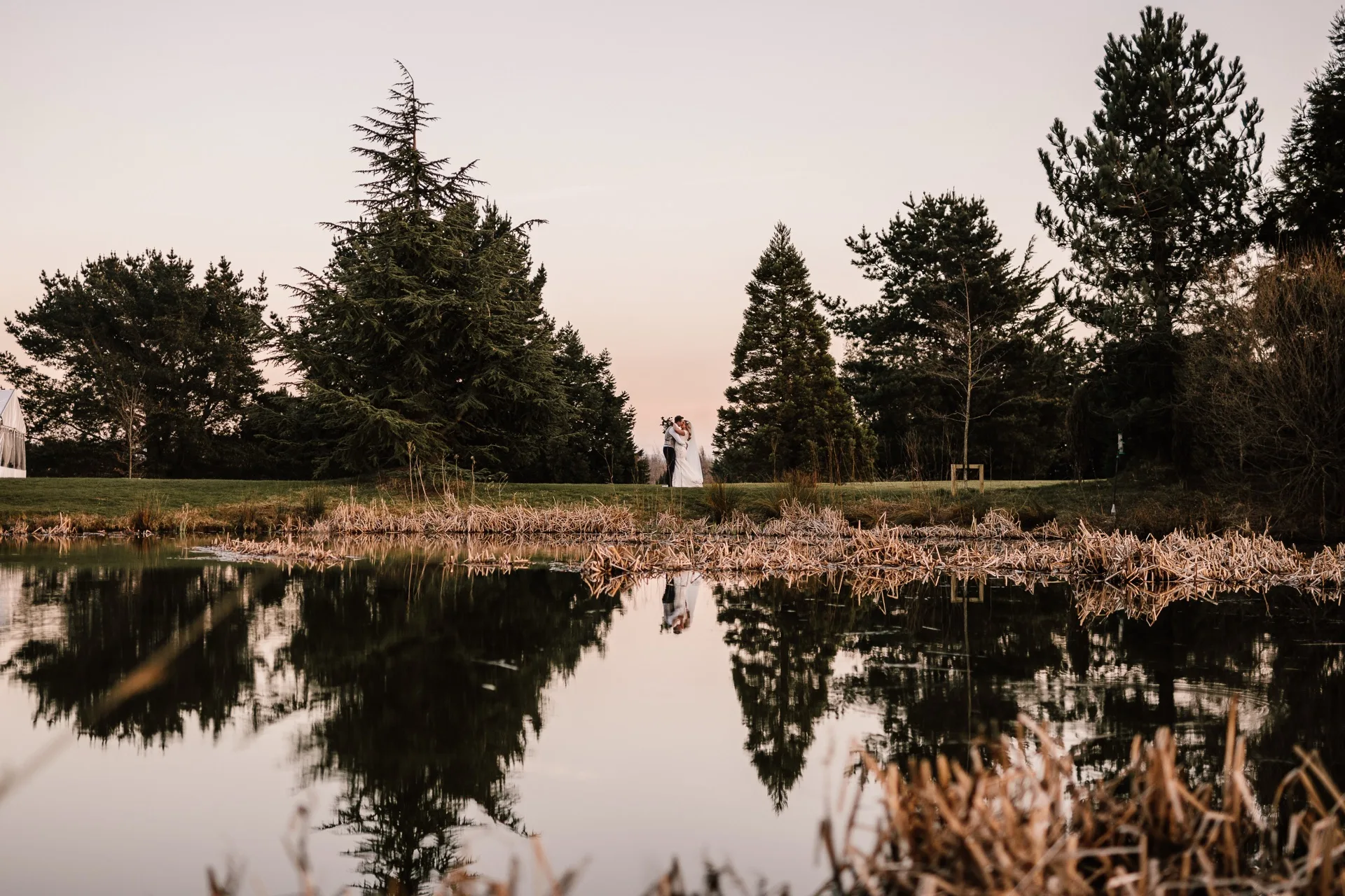 The lake at The Hidden Oak at dusk, with the treeline reflected in the water.