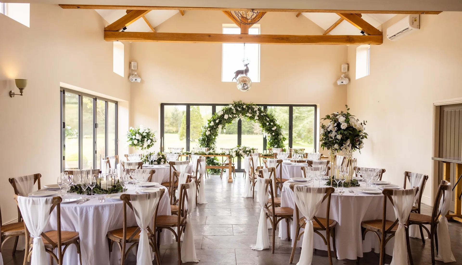 The Barn at The Hidden Oak set for a wedding breakfast, with the ceremony arch beyond.
