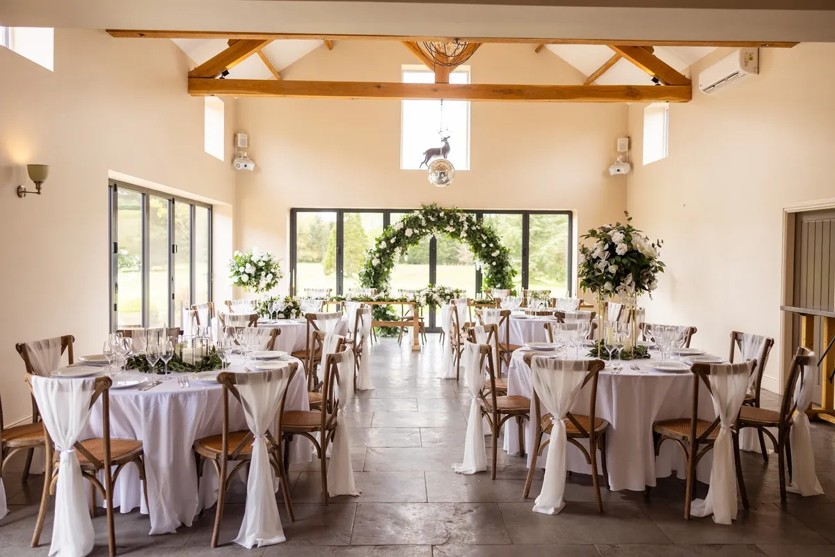Inside the barn at The Hidden Oak, oak beams wrapped in fairy lights above a long table.